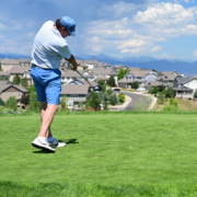 Golfer mid-swing on a vibrant green tee box, captured with crisp motion and a scenic suburban landscape and mountains in the background.